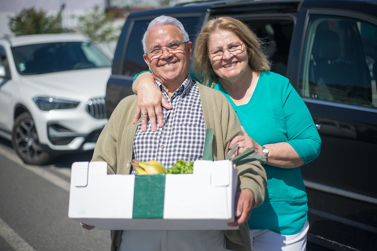senior couple with groceries in front of car